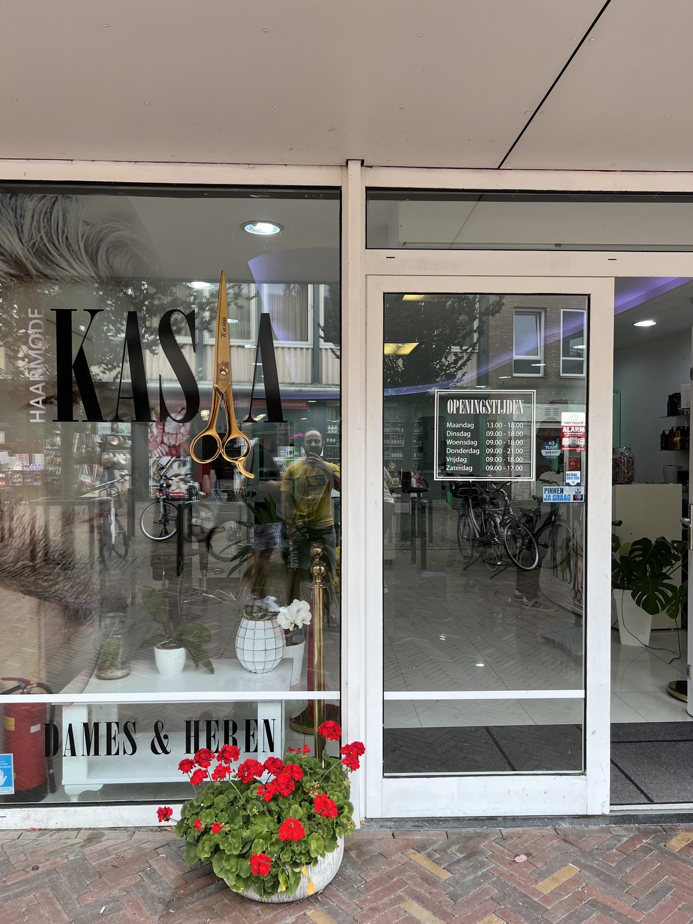 De winkelpui van Haarmode Kasia met KASIA en Dames & Heren op het raam en rode geraniums bij de deur